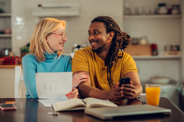 A cheerful affectionate multiracial couple is sitting at home and planning home finances and budget together.