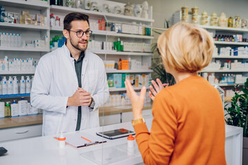 Portrait of a male pharmacist helping a senior woman patient in pharmacy