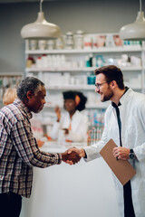 Male pharmacist shaking hands with a senior african american man patient in pharmacy