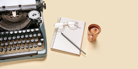 Vintage typewriter with eyeglasses, notebook, pencil and cup of coffee on beige background