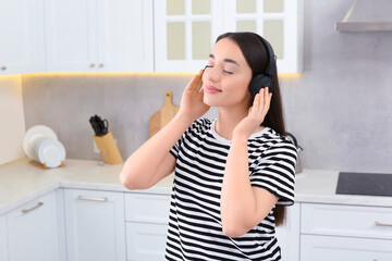 Beautiful woman in headphones enjoying music in kitchen