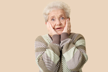 Shocked senior woman on beige background