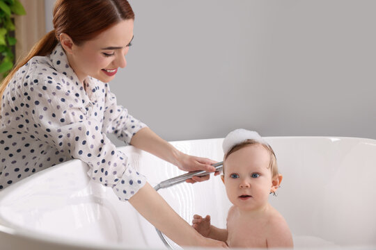Mother washing her little baby in tub at home