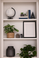 Interior design. Shelves with stylish accessories, potted plants and frame near white wall