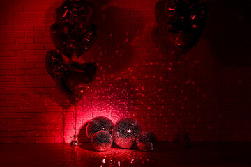 Many shiny disco balls in room decorated with heart shaped balloons, toned in red