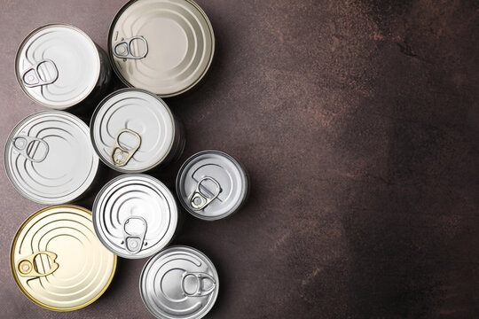 Many closed tin cans on brown table, flat lay. Space for text