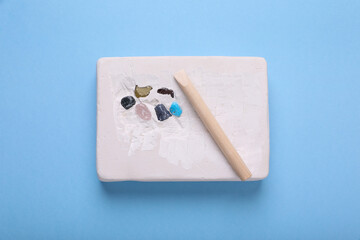 Fototapeta na wymiar Educational toy for motor skills development. Excavation kit (plaster, wooden chisel and gemstones) on light blue background, top view
