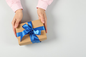 Woman holding gift box on light background, top view. Space for text