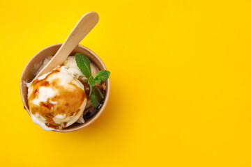 Scoops of ice cream with caramel sauce and mint leaves on yellow table, top view. Space for text