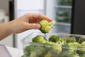 Woman putting green broccoli into glass container in kitchen, closeup. Food storage