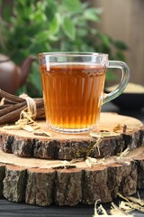 Aromatic licorice tea in cup and dried sticks of licorice root on black wooden table