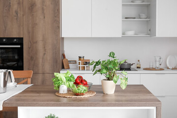 Wooden island table with fresh vegetables and houseplant in modern kitchen
