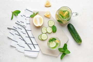 Glass and jug of lemonade with cucumber on white background