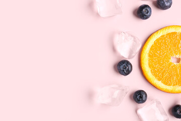 Orange slice with ice cubes and blueberries on pink background