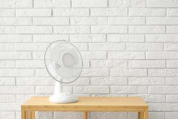 Wooden table with modern electric fan near white brick wall