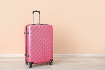 Pink suitcase near pale orange wall. Travel concept
