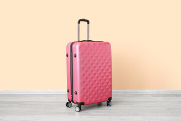 Pink suitcase near pale orange wall. Travel concept