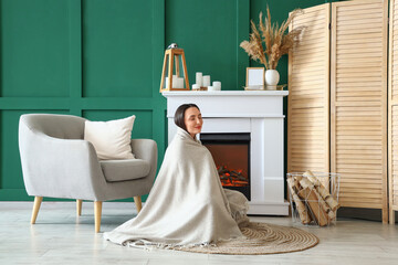 Young woman with plaid sitting near fireplace at home