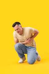 Young man having heart attack on yellow background