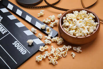 Bowl with tasty popcorn, clapperboard and film reel on brown background