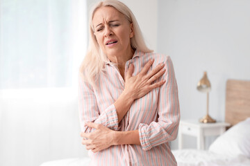 Mature woman having heart attack in bedroom - obrazy, fototapety, plakaty