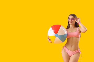 Young woman in swimsuit with beach ball on yellow background