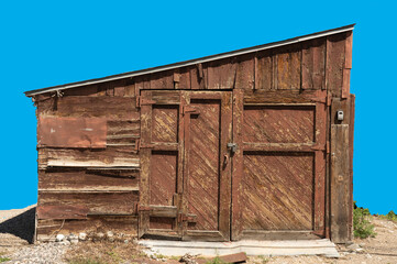 Isolated shack, barn or garage standing locked and boarded up. The  red paint is worn on weathered old wood. Doors & windows are blocked. See gravel at front ground. Text space.