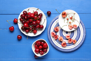 Plates and bowl of sweet cherries on blue wooden background
