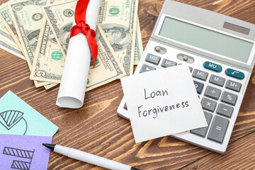 Diploma, dollar banknotes, calculator and sticky note with text LOAN FORGIVENESS on wooden background