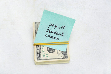 Dollar banknotes and sticky note with text PAY OFF STUDENT LOANS on white background