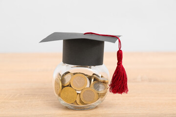 Jar with coins and graduation cap on wooden table against grey background. Student loan concept