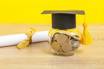 Jar with coins, graduation cap and diploma on wooden table against yellow background. Student loan...