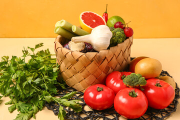 Wicker basket with different fresh fruits and vegetables on yellow table