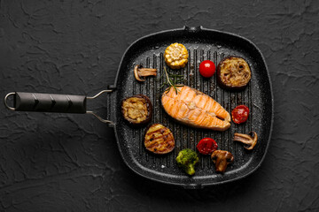 Frying pan with tasty grilled salmon steak and vegetables on black background