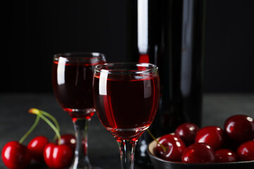 Glasses and bottle with sweet cherry liqueur on black background