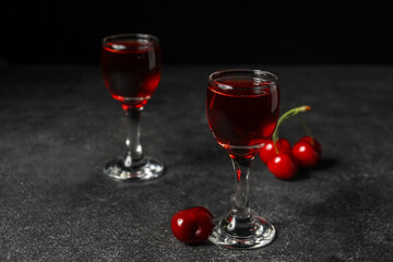 Glasses with sweet cherry liqueur on black background
