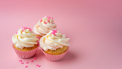 Vanilla cupcakes with cream cheese frosting and pink sprinkles on pink background. Saint Valentine's day or birthday dessert. Beautiful festive food for wedding or baby shower girl. Copy space.