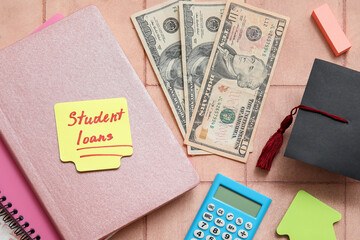Sticky note with text STUDENT LOANS, dollar banknotes, calculator, notebook and graduation cap on tiled background