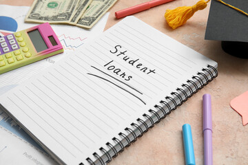 Notebook with text STUDENT LOANS, dollar banknotes and stationery on beige table