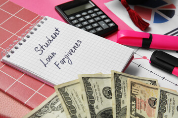 Notepad with text STUDENT LOAN FORGIVENESS, calculator, markers and dollar banknotes on pink background