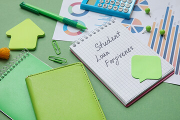 Notepad with text STUDENT LOAN FORGIVENESS, calculator, charts and stationery on green background