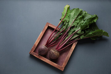 Fresh beetroot with leaves in wooden plate on grey background