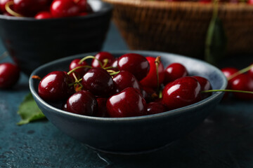 Bowl with sweet cherries on blue background