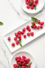 Plates with fresh raspberries and mint on white background