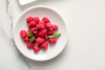 Plate with fresh raspberries and mint on white background