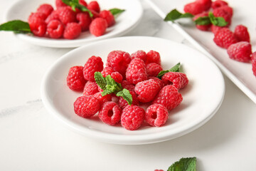 Plates with fresh raspberries and mint on white background