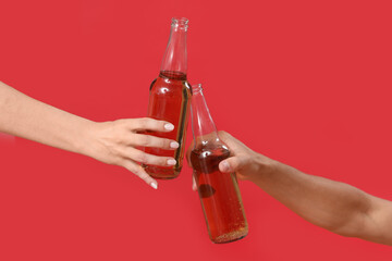 Young man and woman with beer clinking on red background, closeup