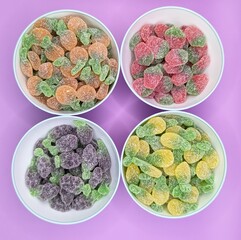 Four recipients, each one with a different type of fruit gummy on purple background