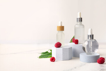 Obraz na płótnie Canvas Decorative podiums with bottles of cosmetic raspberry oil on white background