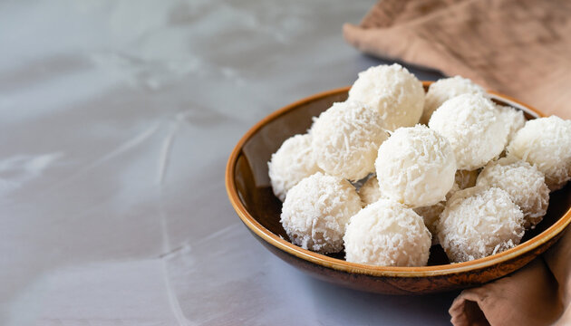 Coconut balls, raw and healthy sugar free rafaello candies. Vegetarian energy sweets recipe step by step. Round tasty dessert in ceramic bowl. Copy space, close up view. Healthy organic food for kids.